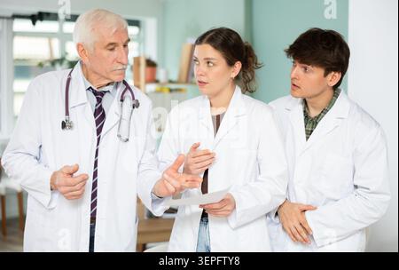 Drei professionelle Ärztinnen und Ärztinnen im weißen medizinischen Mantel diskutieren und erklären Ergebnisse der ärztlichen Untersuchung in der Arztpraxis in der Klinik Stockfoto