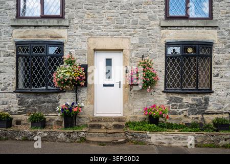 Detaillierte architektonische Ansicht mit Schwerpunkt auf den Steinfensterrahmen, Bleiglasfenstern und hängenden Blumenkörben eines traditionellen Steinhauses auf Th Stockfoto