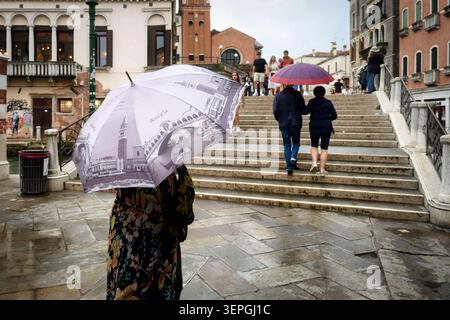 Venedig, Italien 02. Juni 2026: Eine Person mit einem stilisierten venezianischen Souvenirschirm steht an einem regnerischen Tag in Venedig, I, vor der historischen Steinbrücke Stockfoto