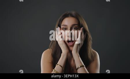 Eine junge Frau, die erstaunt und schockiert mit Händen im Gesicht aussieht, die starke Emotionen ausdrücken Stockfoto