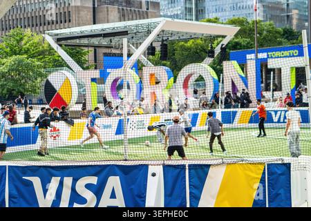 Toronto, Kanada – 14. Juni 2026: Eine Gruppe verschiedener junger Männer, darunter asiatische, schwarze und weiße Spieler, nehmen an einem interaktiven Mini-Football-Turnier am Nathan Phillips Square teil. Während des Dribbels in der Mitte der Action und beim Passieren eines Fußballballs auf einem Pop-up-Feld spielen sie vor der Kulisse der berühmten Toronto City Hall. Umgeben von einem lebhaften Turnier-Branding zeigt diese lebhafte Szene ein intensives Fan-Engagement und Gemeinschaftsgeist während der offiziellen FIFA-Weltmeisterschaft 2026 in Toronto. Stockfoto
