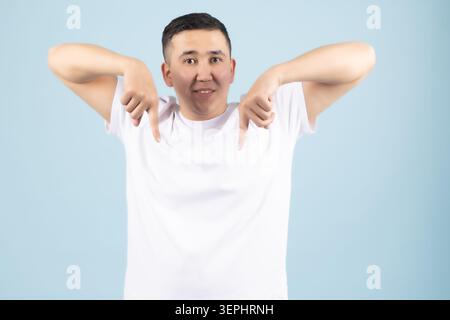 Junger Mann, der beide Zeigefinger mit einem komischen Ausdruck nach unten zeigt Stockfoto