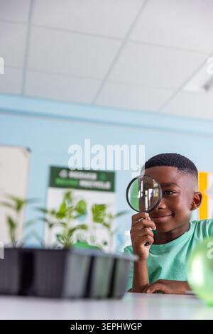 Afroamerikanischer Schuljunge, der Lupe hält, Setzlinge am Klassentisch untersucht, Kopierraum Stockfoto