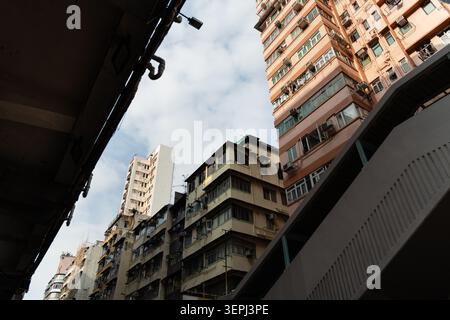 Tiefwinkelblick auf dicht gepackte alte Wohnhäuser mit Klimaanlagen und Balkonen vor teilweise bewölktem Himmel in Mong Kok, Kowl Stockfoto