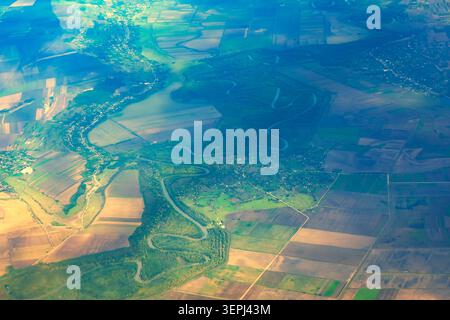 Aus der Vogelperspektive auf einen sich schlängelnden Fluss, der sich durch eine ausgedehnte landwirtschaftliche Landschaft schlängelt, mit Flickenteppelfeldern und kleinen Siedlungen Stockfoto