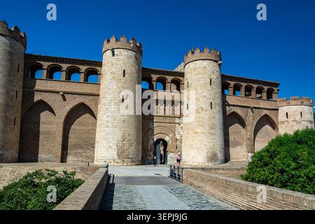 Saragossa, Spanien - 17. August 2022: Ein Besucher nähert sich dem befestigten Eingang und den runden Türmen des Aljaferia-Palastes unter einem klaren blauen Himmel. Stockfoto