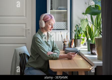 Lächelnde reife Frau im Kopfhörer, die Musik-Playlist auf der Online-Abonnementplattform anhört. Stockfoto