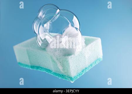 Hellblauer Reinigungsschwamm mit Schaum- und Seifenblasen auf blauem Hintergrund. Hausarbeit oder Reinigungsdienste von zu Hause.Reinigungsbedarf Konzept. Stockfoto