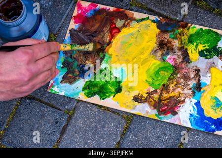 Künstler mischt Acrylfarbe auf einer Holzpalette auf Kopfsteinpflaster im Freien. Stockfoto