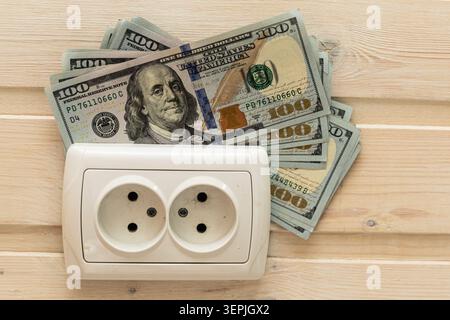 Steckdose mit 100-Dollar-Banknoten, die die steigenden Energiekosten der Haushalte symbolisieren Stockfoto