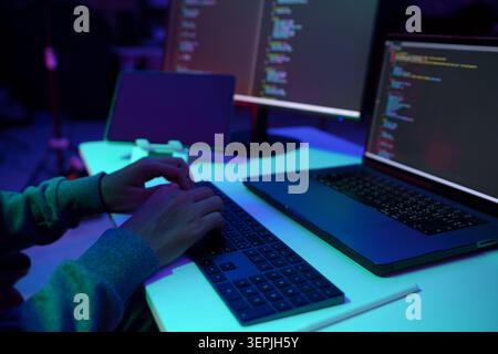 Programmierer, der Code auf dem Laptop in Neon lit Workspace eingibt Stockfoto