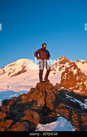 Der Wanderer steht auf einem felsigen Bergrücken mit schneebedecktem Vulkan dahinter. Stockfoto