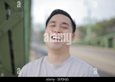 Junger asiatischer Mann lacht fröhlich auf einer Brücke Stockfoto
