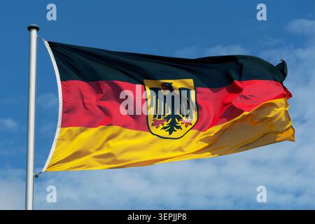 Deutsche Flagge auf einem Fahnenmast schwenken, mit dem Bundeswappen (Bundesadler) in der Mitte Stockfoto