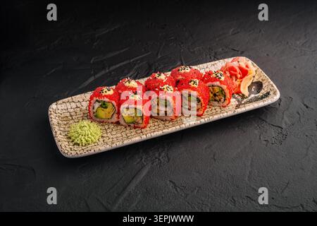 Sushi-Brötchen sind ordentlich auf einem Teller angeordnet. Die Brötchen haben rote Beläge und zeigen eine Füllung mit Gemüse und Fisch. Wasabi und eingelegter Ingwer werden als Gewürze beiseite gelegt. Stockfoto
