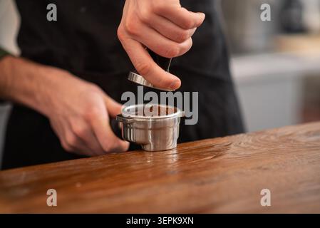 Eine Nahaufnahme eines Barista, der gemahlenen Kaffee mit einem Metallmanipulator in einen Portafilter drückt Stockfoto
