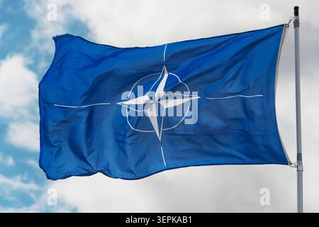 Die NATO-Flagge auf einem Fahnenmast vor bewölktem Hintergrund schwenken Stockfoto