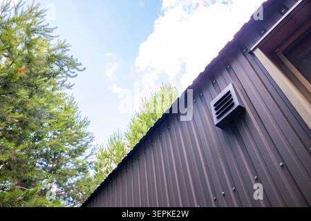 Lüftungsgitter auf Wellblechwand eines modernen Vorstadthauses. Konzept: Lüftungssysteme Stockfoto