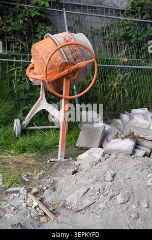 Orangefarbener Betonmischer neben dem Holzblock auf der Baustelle im Hinterhof Stockfoto