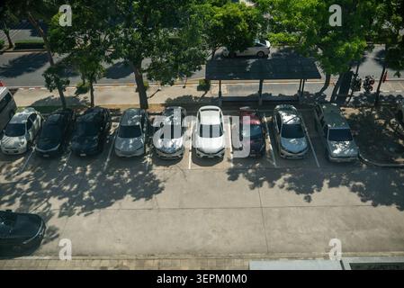 Ein Luftbild, das einen Parkplatz zeigt, der von Bäumen gesäumt ist, die Schatten spenden, mit verschiedenen Fahrzeugen gefüllt sind und die städtischen Verkehrsmittel und Outdoorbereiche hervorheben Stockfoto
