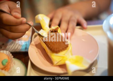 Eine Person wird gesehen, wie sie gelbe Kuchenwickel um einen rechteckigen Brownie auf einem rosafarbenen Teller faltet und dabei Backhandwerkskunst und Dessertkreation in einer gemütlichen Atmosphäre zeigt Stockfoto