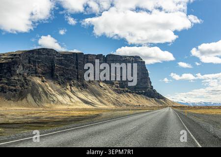 Asphaltierte Straße Route 1 führt in Richtung der hoch aufragenden Lómagnúpur-Bergklippe in Island Stockfoto