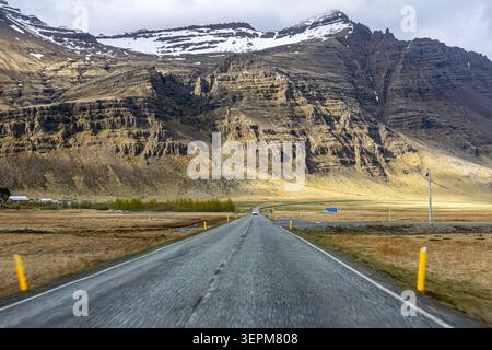 Asphaltstraße, die in Richtung schneebedeckter Berge unter bedecktem Himmel auf der Ringstraße bei Hofn Island führt Stockfoto