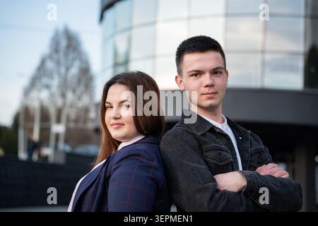 Junge Geschäftsleute, die hinter einem modernen Bürogebäude an einem städtischen Arbeitsplatz stehen. Unternehmensführung und Teamarbeit für Karriereplanung Stockfoto