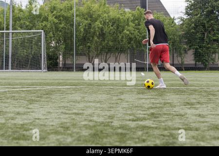 Ein männlicher Fußballspieler trainiert auf einem Fußballfeld und konzentriert sich auf Ballkontrolle und Schießübungen, umgeben von grünem Gras und Torpfosten. Stockfoto