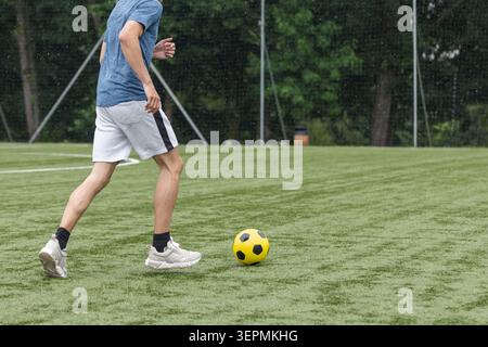 Ein junger Athlet übt auf einem Fußballfeld mit einem gelben Ball Fußballfähigkeiten aus. Die Sitzung konzentriert sich auf Ballkontrolle und Schießübungen. Stockfoto