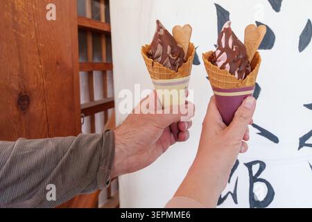 Zwei Hände halten Milcheis-Waffelkegel mit Schokolade Stockfoto