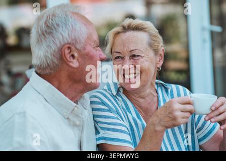 Lächelndes älteres Paar, das im Garten Kaffee genießt. Stockfoto