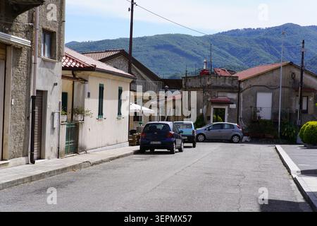 Straßenszene mit geparkten Autos und traditionellen Häusern mit grünen Bergen im Hintergrund in Molochio, Kalabrien an einem sonnigen Tag in Süditalien. Stockfoto