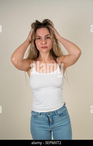 Junge Frau, die lange blonde Haare mit beiden Händen in einem Studio zieht Stockfoto