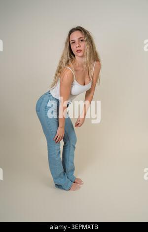 Junge Frau mit langen blonden Haaren posiert selbstbewusst in einem minimalistischen Studio-Setting Stockfoto