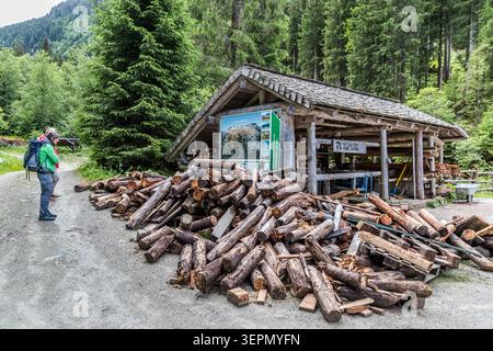 Walker stehen vor einer Hütte mit einer Nationalpark-Informationstafel und einem großen Holzstapel am Rundweg Untersulzbach-Wasserfall. Hütten wie diese dienen als Rastplätze und bieten Schutz vor dem Wetter im Nationalpark Hohe Tauern. Rosental, Neukirchen am Großvenediger, Bezirk Zell am See, Salzburg, 5741, Österreich Stockfoto