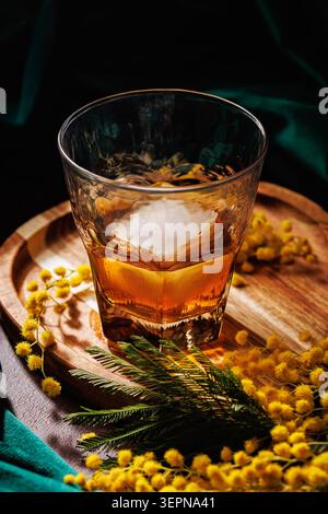 Amber Whiskey mit Eis und Mimosa Blumen auf Holztablett Stockfoto