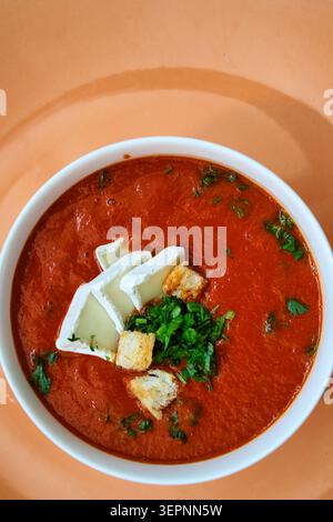 Cremige Pfeffer- und Tomatensuppe mit Brie-Käse, Croutons und frischer Petersilie in einer weißen Schüssel, von oben fotografiert. Stockfoto