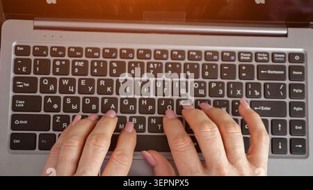 Weibliche Hände mit rosafarbenen Nägeln, die auf einer Laptop-Tastatur am Schreibtisch tippen, Nahansicht von oben, die fokussierte digitale Arbeit, Kommunikation und Fernbedienung zeigt Stockfoto