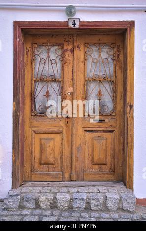 Verwitterte Doppeltür aus Holz mit schmiedeeisernen Panels und Nummer 4 über rustikalem Eingang Stockfoto