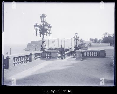 In Monte-Carlo steht ein Mann auf einer erhöhten Terrasse mit Brüstungen, Straßenlaternen und Bänken und überblickt die Mittelmeerküste und das Stadtbild des Resorts während der Erweiterung und der Freizeitgestaltung der Belle Epoque 1905. Stockfoto