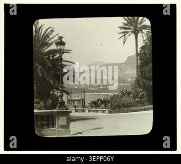 Ascenseur de la gare in Monte-Carlo, Monaco im Jahr 1859 präsentiert ein Bahnhofsaufzugssystem, das die Bahnhöfe mit angrenzenden Umlaufbereichen verbindet, eingerahmt von Brüstungen, Leuchten und palmengesäumtem Küstengelände mit Blick auf den mediterranen Hang. Stockfoto