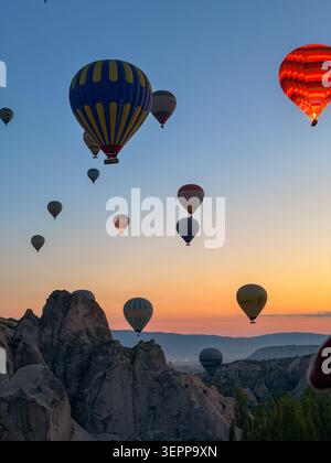 Farbenfrohe Heißluftballons erfüllen den Himmel über Kappadokiens einzigartiger Landschaft bei Sonnenaufgang. Stockfoto