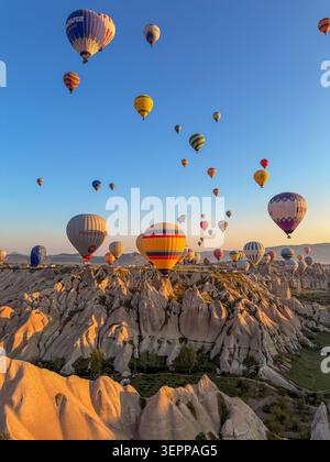 Ein atemberaubender Blick auf farbenfrohe Heißluftballons, die bei Sonnenaufgang über die einzigartigen Felsformationen Kappadokiens fliegen. Stockfoto