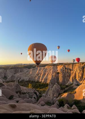 Diese atemberaubende Szene zeigt farbenfrohe Heißluftballons, die bei Sonnenaufgang über den einzigartigen Felsformationen Kappadokiens treiben. Stockfoto