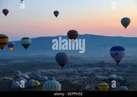 Ein atemberaubender Blick auf farbenfrohe Heißluftballons, die während des Sonnenaufgangs über die einzigartige Landschaft Kappadokiens schweben. Stockfoto