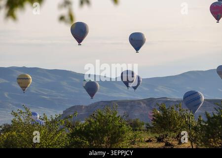 Farbenfrohe Heißluftballons schweben anmutig über die malerischen Hügel Kappadokiens und bieten eine atemberaubende Aussicht. Stockfoto