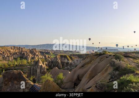 Ein atemberaubender Blick auf farbenfrohe Heißluftballons, die während des Sonnenaufgangs über den einzigartigen Felsformationen Kappadokiens fliegen. Stockfoto