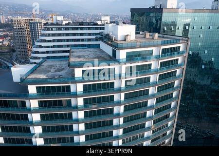 Blick aus der Luft moderner Wohnkomplex mit blauen Glasbalkonen auf der Dachterrasse, städtische Skyline, Entwicklung von Luxusobjekten, Wachstum von Bauten, Berglandschaft. Stockfoto