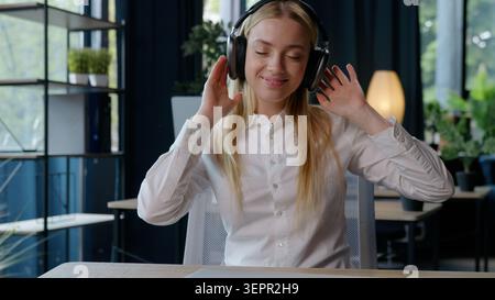 Fröhlich lächelnde kaukasische Geschäftsfrau mit Telefon, das Kopfhörer trägt, Musik Musik hören, Lied hören, Audio hören im Büro Geschäftsfrau lächeln gut genießen Stockfoto